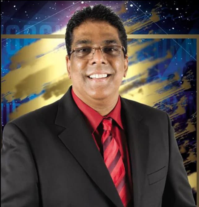 Dr RJ Sing smiling, in a dark suit and red tie